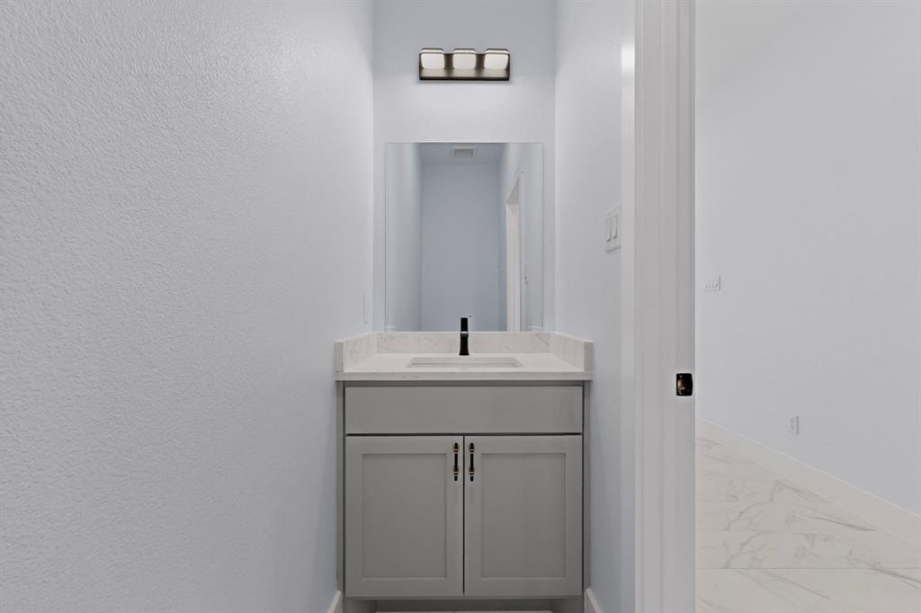Powder room featuring a single vanity with gray cabinetry, a rectangular undermount sink, and a light-toned countertop