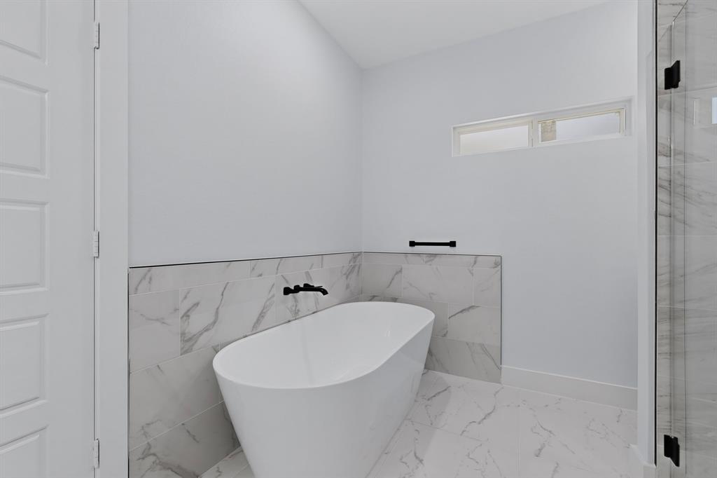 Freestanding soaking tub with matte black fixtures, marble-look tile surround, and a clear glass shower enclosure