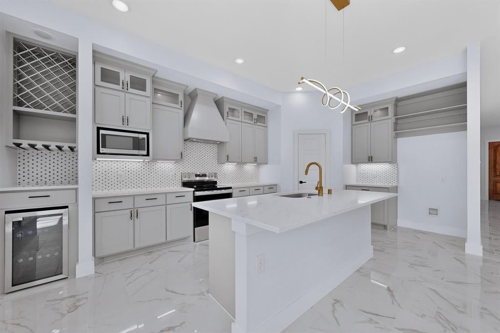 Kitchen featuring a central island with an integrated sink, light-toned cabinetry, stainless steel appliances, a geometric tile backsplash, and polished tile flooring Kitchen featuring a central island with an integrated sink, light-toned cabinetry, stainless steel appliances, a geometric tile backsplash, and polished tile flooring