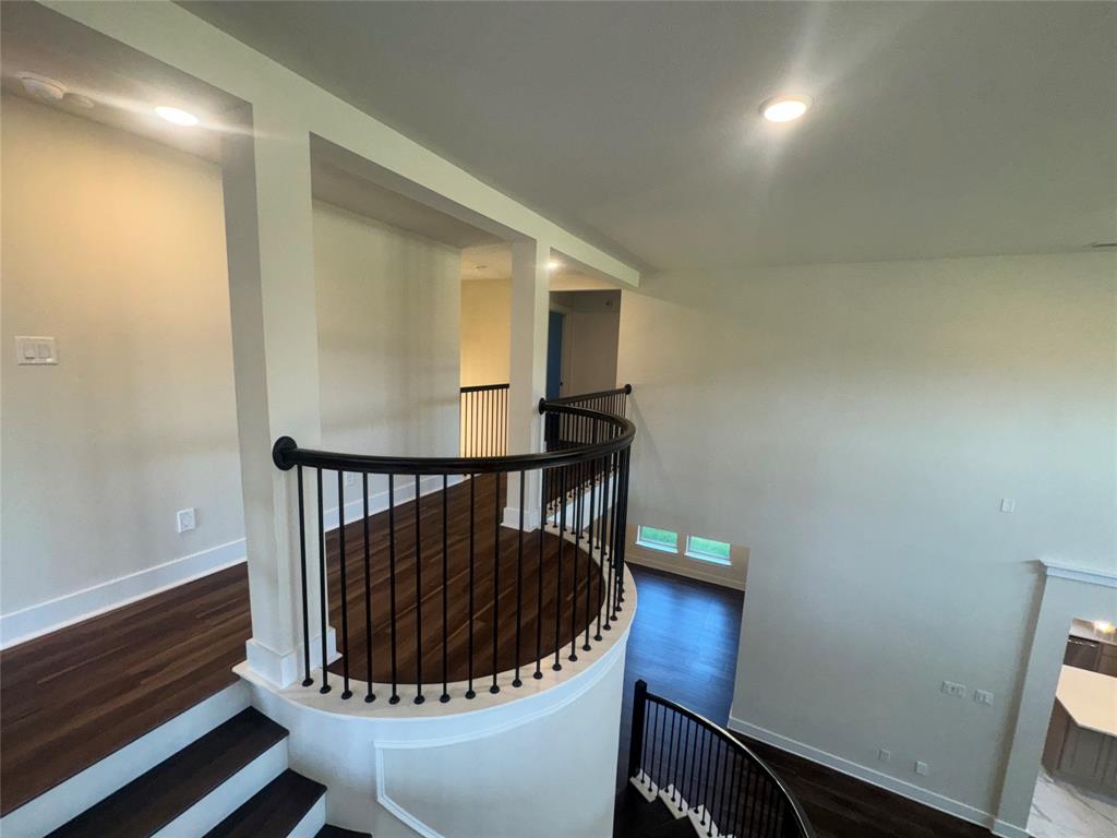 Curved staircase with black wrought iron balusters, wood-finish flooring, recessed lighting, and a neutral color palette