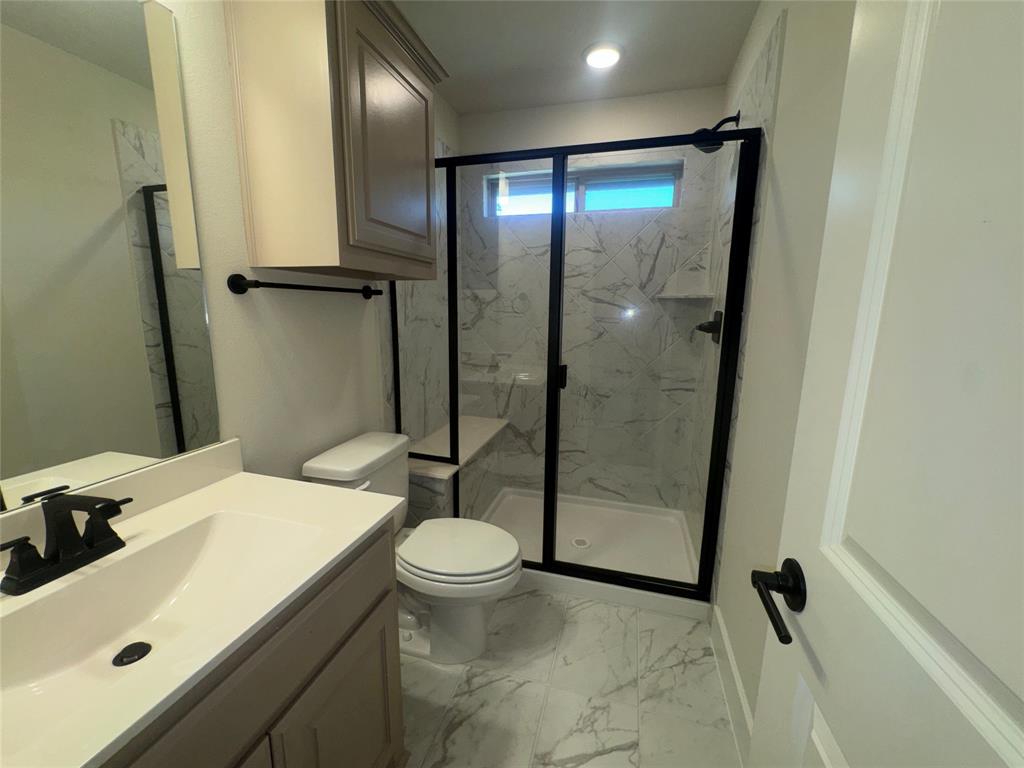 Walk-in shower with black-framed glass enclosure, integrated bench, and marble-patterned tile surround Walk-in shower with black-framed glass enclosure, integrated bench, and marble-patterned tile surround