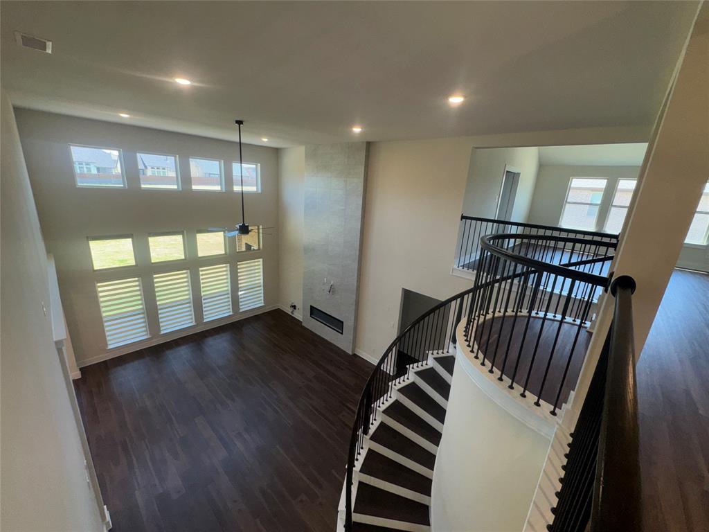 Two-story ceiling, large windows with horizontal blinds, built-in fireplace, dark wood-finish flooring, and a spiral staircase with metal balusters