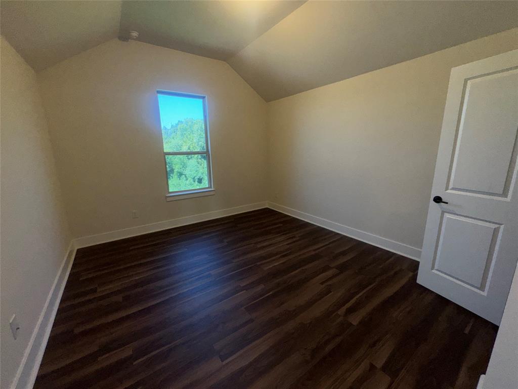 Vaulted ceiling, wood-finish flooring, white trim, single window, and a paneled door with matte black hardware Vaulted ceiling, wood-finish flooring, white trim, single window, and a paneled door with matte black hardware