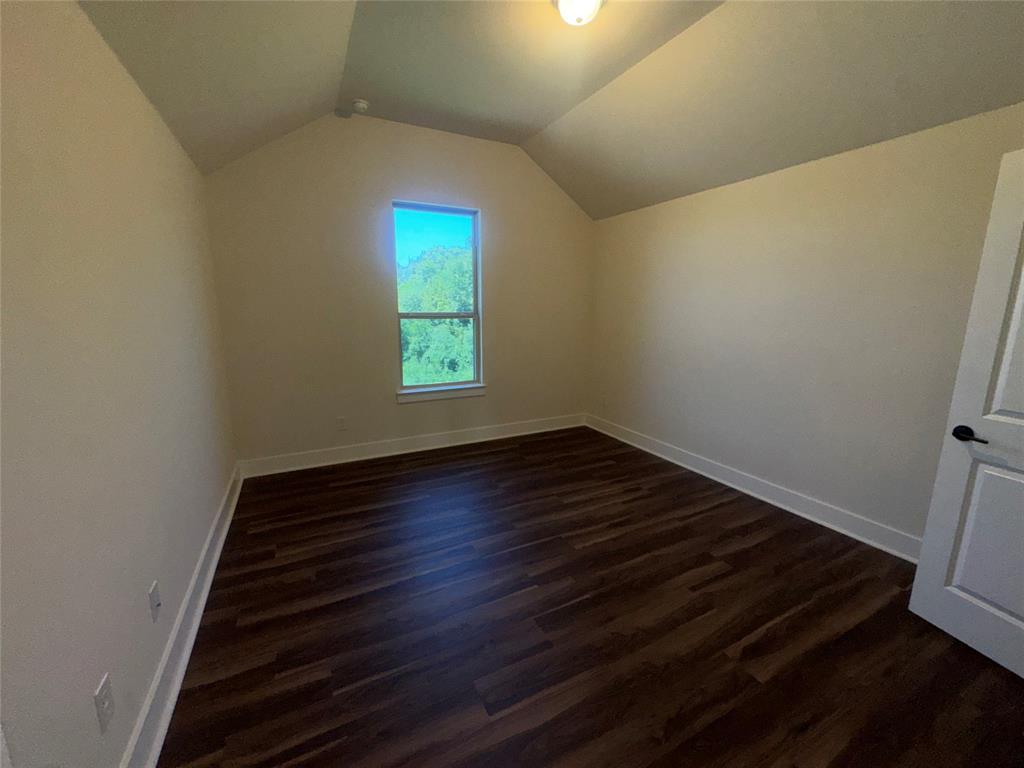 Wood-finish flooring, single window, white trim, attic-style sloped ceiling, and a paneled door with dark hardware
