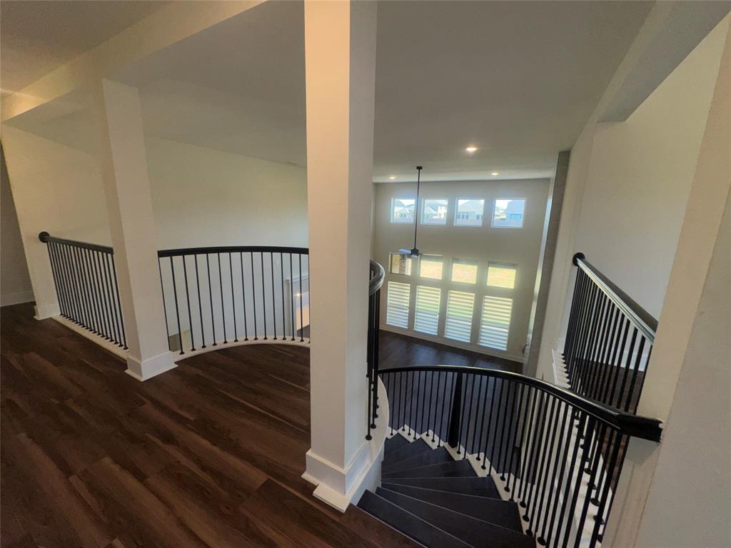 Open concept interior with wood-finish flooring, two-story windows with plantation shutters, a curved staircase with black metal balusters, and recessed lighting