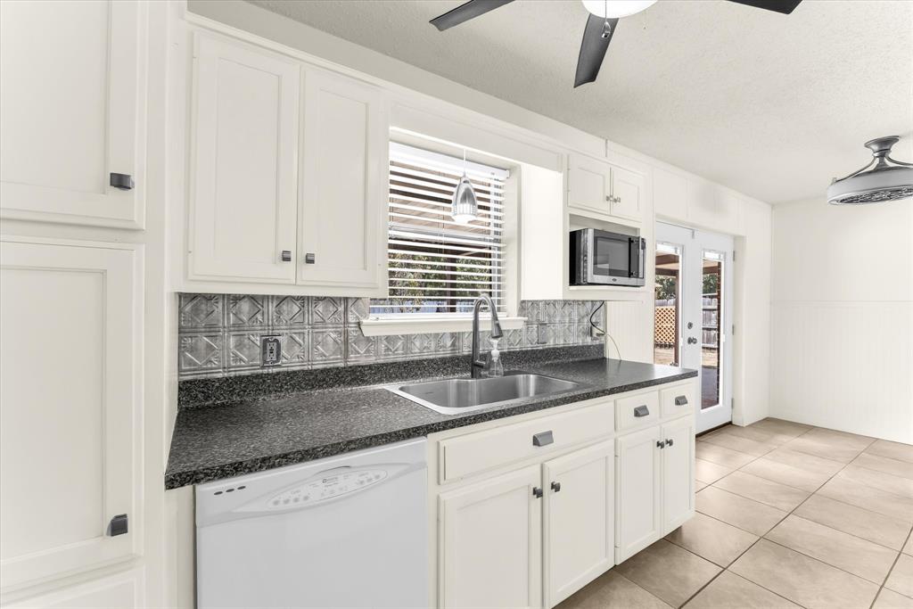White cabinetry, dark stone-finish countertops, stainless steel sink, patterned tile backsplash, and light-toned tile flooring