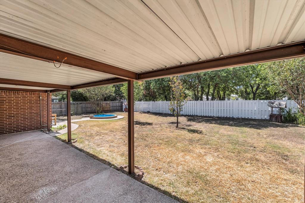 Covered patio with concrete flooring, brick exterior wall, and white picket fencing