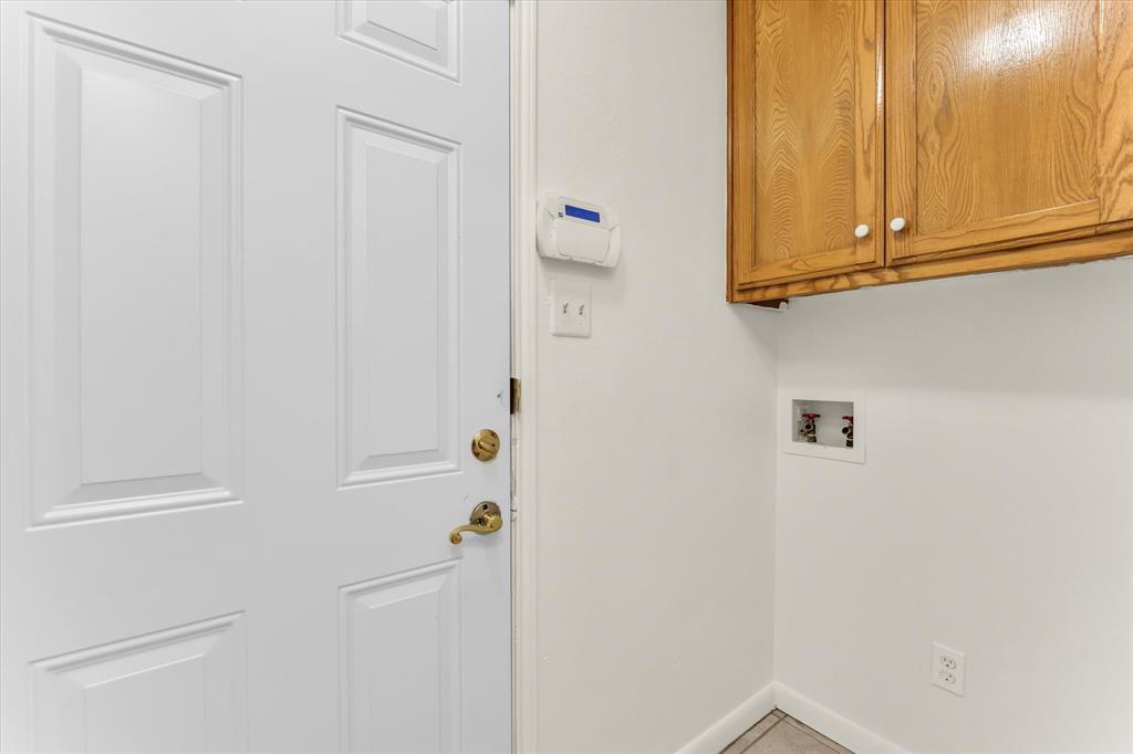 Utility area with light wood-finish cabinetry, white walls, and tiled flooring