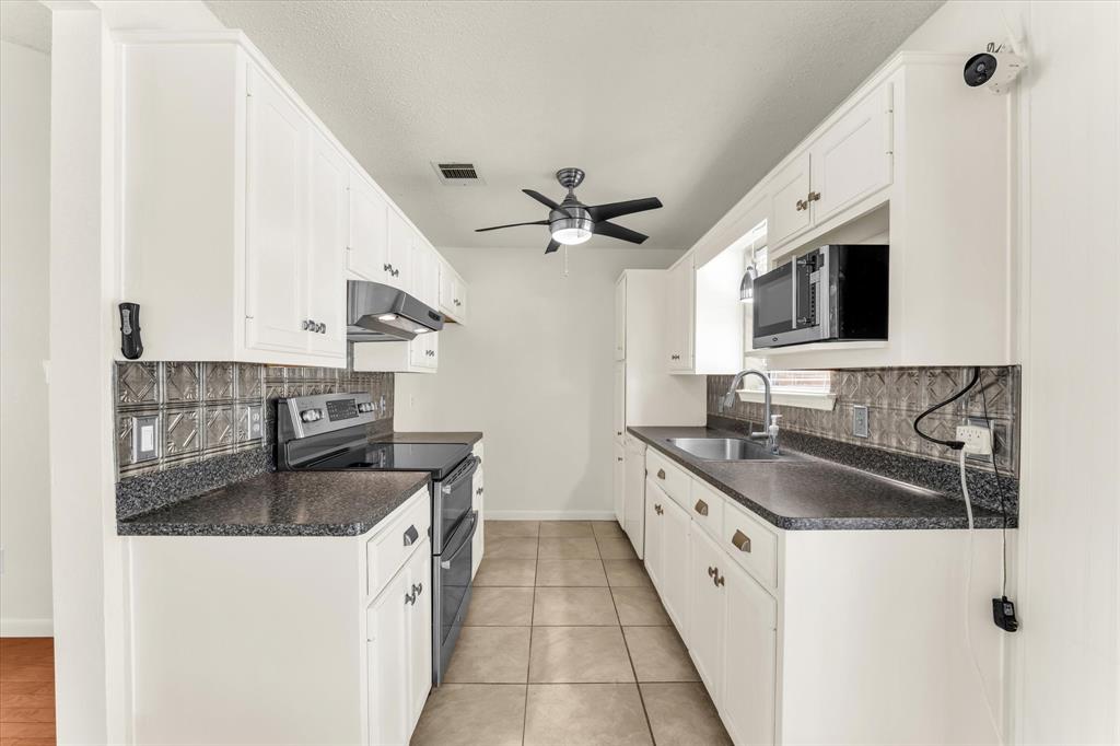 White cabinetry with gold-tone hardware, dark countertops, and a decorative tile backsplash