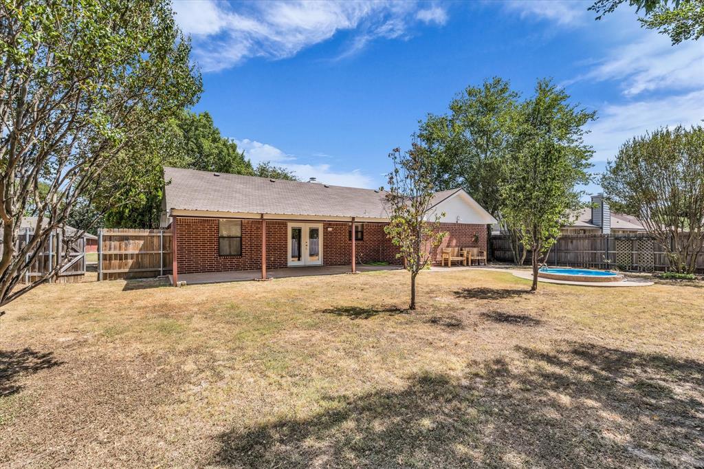 Red brick exterior with a covered patio, double glass doors, and a fenced perimeter