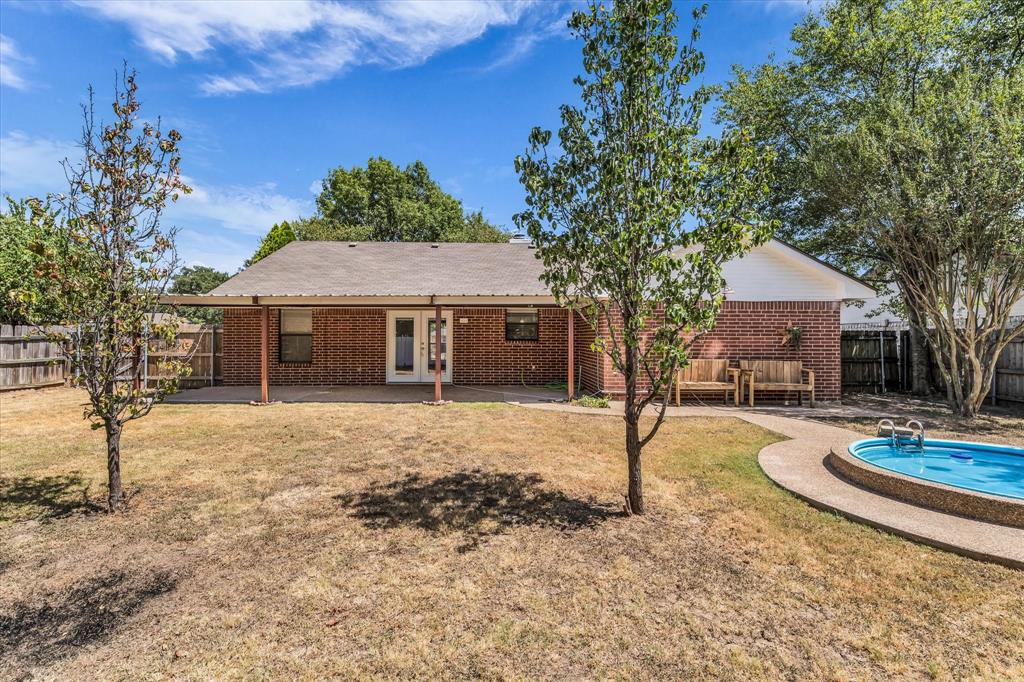 Brick exterior with covered patio, fenced yard, and an in-ground swimming pool