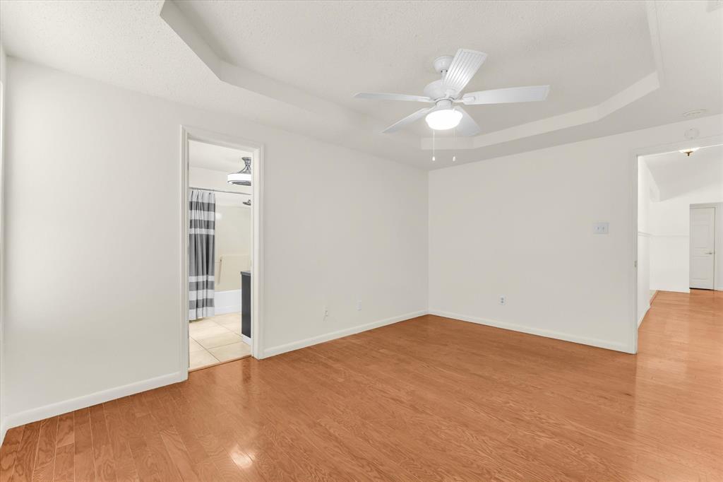 Tray ceiling with a ceiling fan, light wood-finish flooring, and white walls
