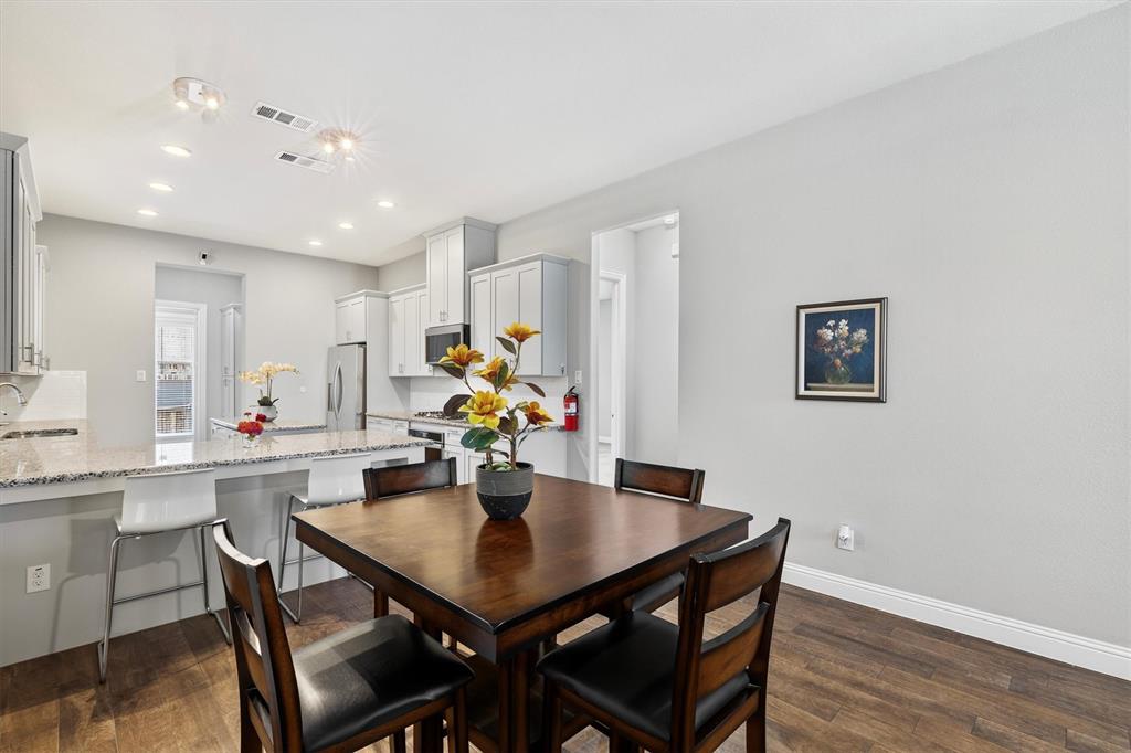 Open-concept kitchen and dining area featuring light-toned cabinetry, stainless steel appliances, and a breakfast bar with stone-finish countertops