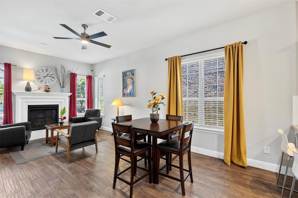 Living area with wood-finish flooring, a ceiling fan, and a fireplace with a white mantel