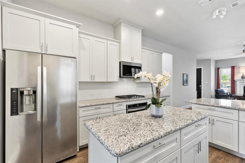 Kitchen featuring white cabinetry, stainless steel appliances, speckled stone countertops, a tile backsplash, and wood-finish flooring