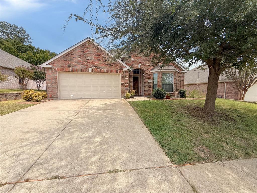 Brick exterior with an integrated garage, concrete driveway, and mature landscaping