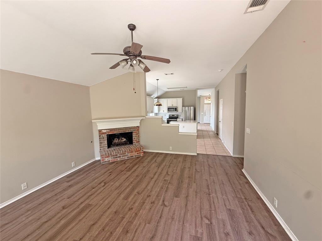 Spacious living area featuring wood-finish flooring, a brick fireplace with a white mantel, and a ceiling fan
