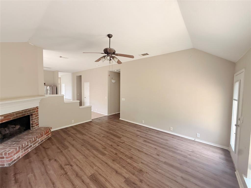 Vaulted ceiling with a ceiling fan, brick-clad fireplace, wood-finish flooring, and a glass-paneled door