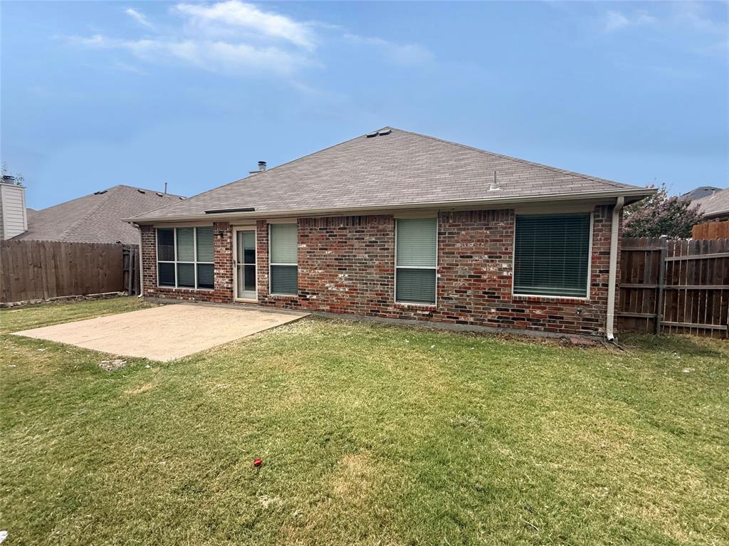 Brick exterior with multiple windows, a concrete patio, and a fenced perimeter