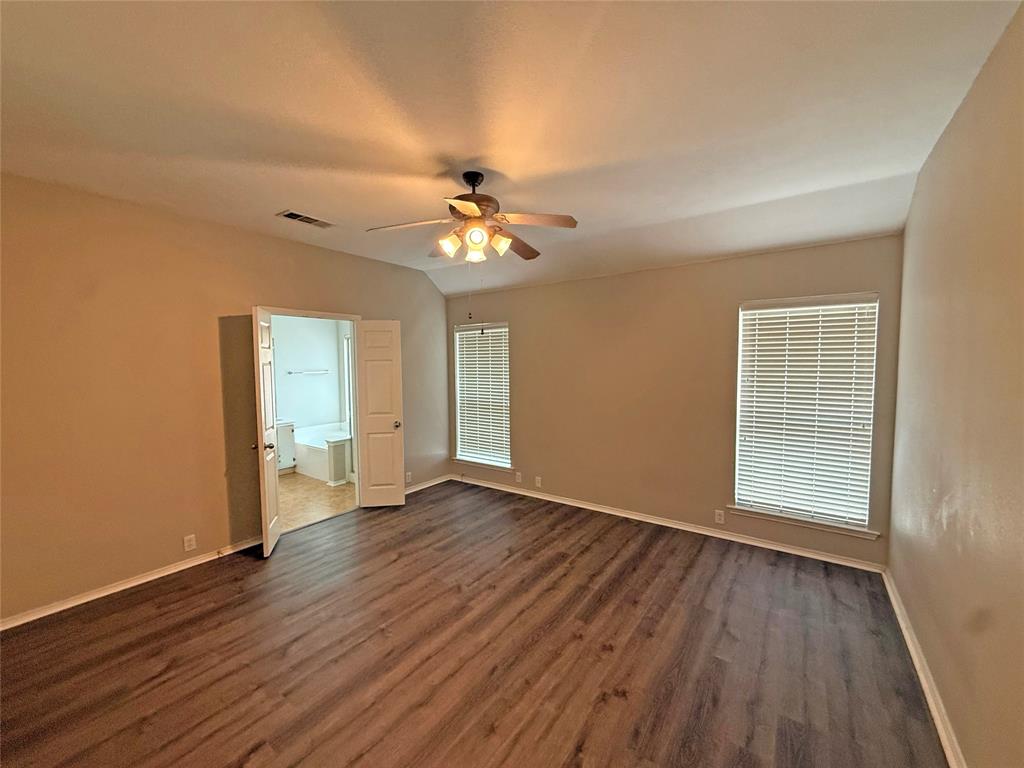 Spacious room with wood-finish flooring, vaulted ceiling, and two windows with blinds