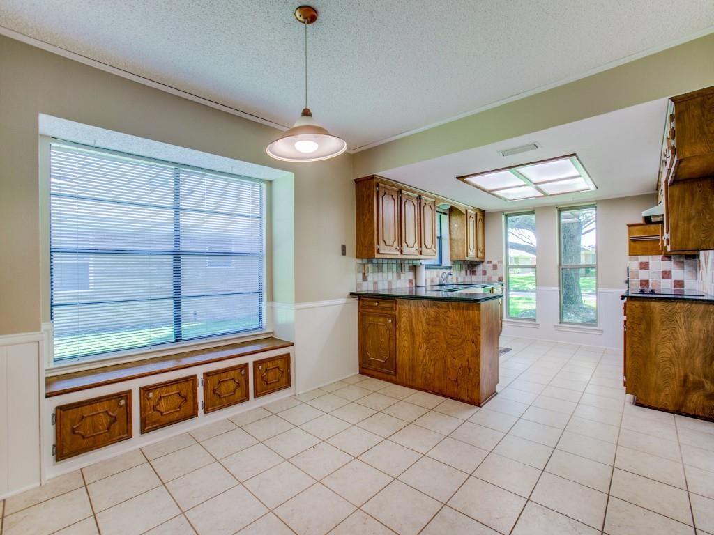 Kitchen featuring light-toned tile flooring, wood-finish cabinetry, dark countertops, and a decorative tile backsplash