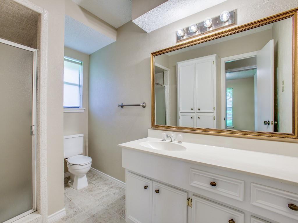 Bathroom featuring a white vanity with integrated sink, a large framed mirror, a four-light fixture, and a glass-enclosed shower