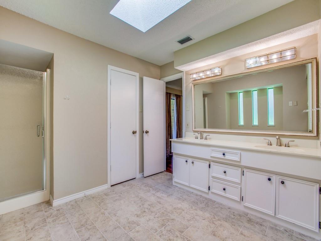 Skylight-equipped bathroom featuring a dual vanity with undermount sinks, a framed mirror, and a glass-enclosed shower