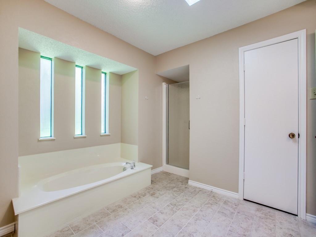 Recessed garden tub with three vertical opaque windows, enclosed shower, and neutral-toned tile flooring