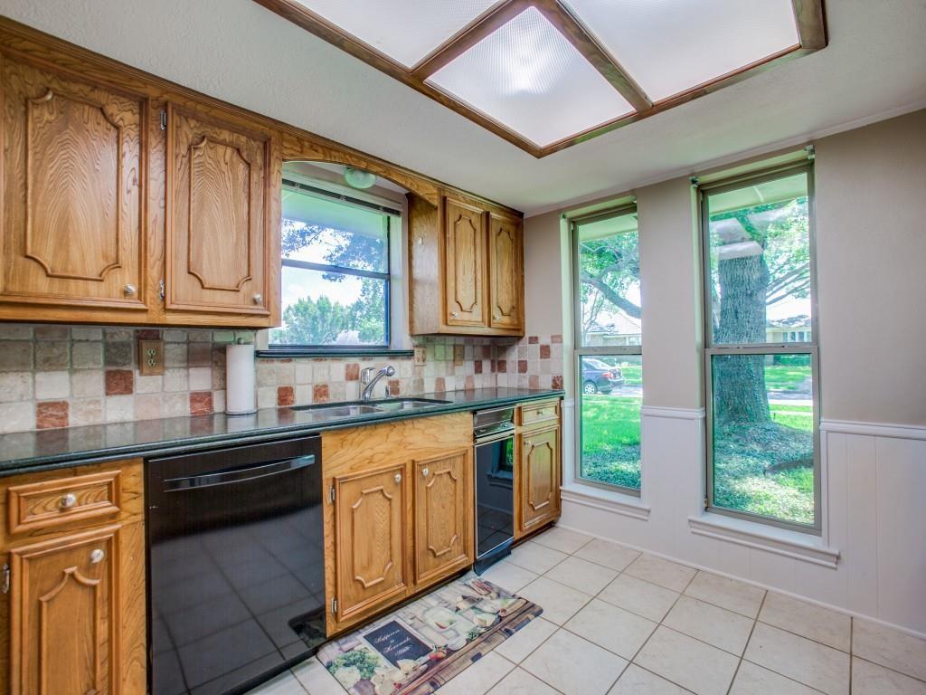 Wood cabinetry with panel detailing, integrated dishwasher, tile backsplash, and dark countertops