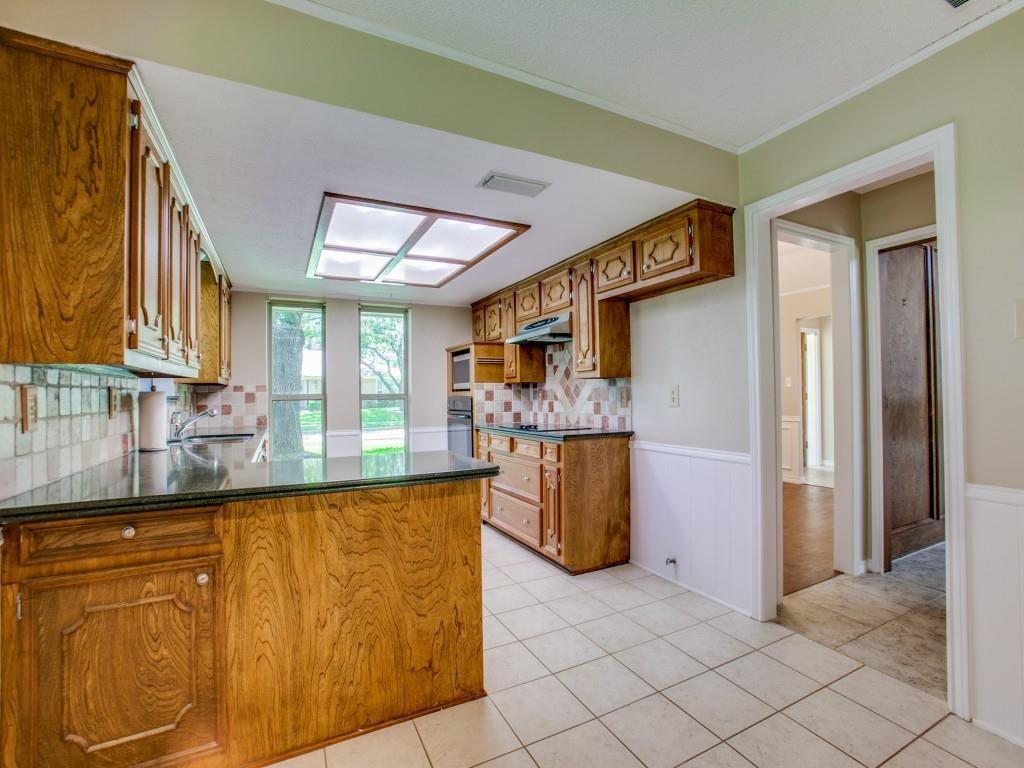 Kitchen featuring wood cabinetry, dark countertops, tiled flooring, a tiled backsplash, and a large skylight