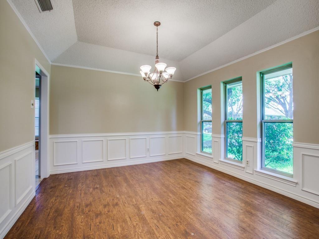 Tray ceiling with crown molding, wood-finish flooring, white wainscoting, and a multi-light chandelier