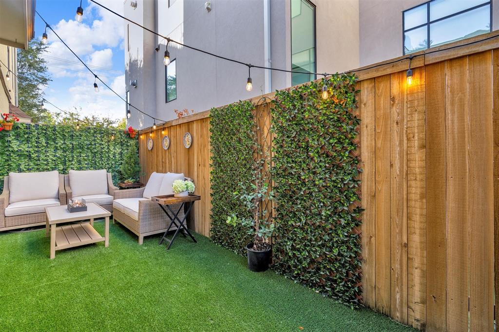 Fenced outdoor area featuring artificial turf, string lighting, and vertical foliage panels