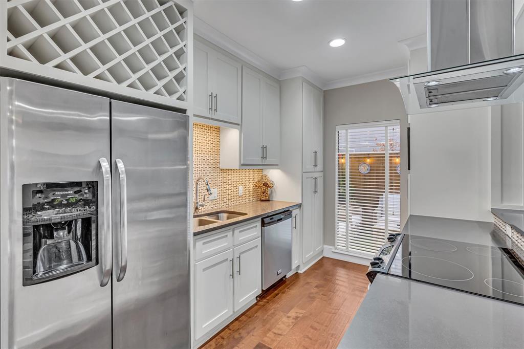 Stainless steel appliances, built-in wine rack, light wood-finish flooring, white cabinetry with silver hardware, and a stone countertop