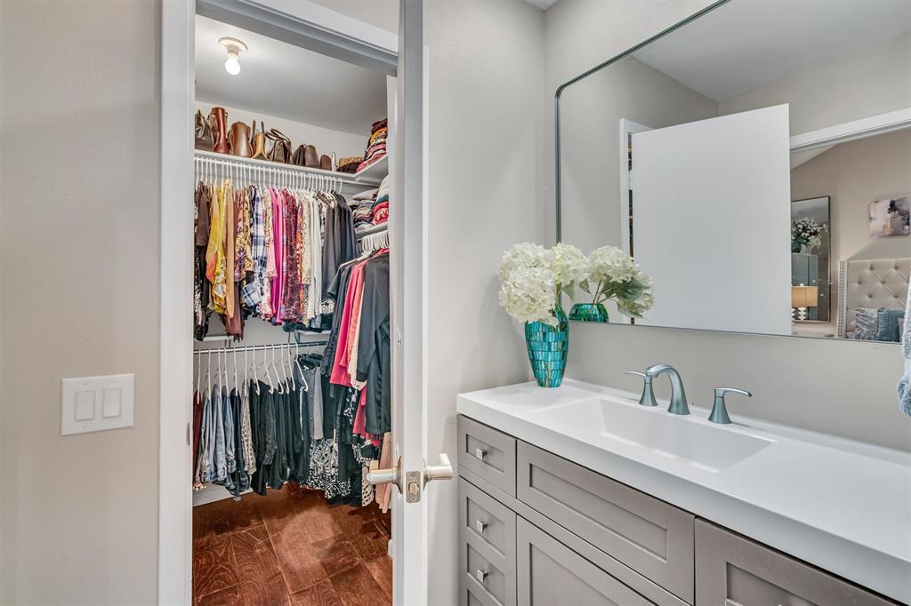 Vanity with integrated sink and chrome fixtures, framed mirror, and walk-in closet with shelving and wood-finish flooring