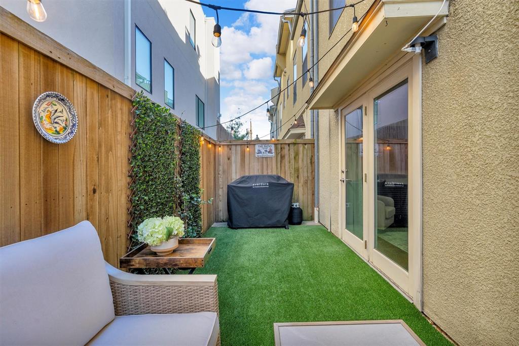 Private outdoor space featuring artificial turf, tall wood fencing with integrated greenery, and exterior lighting