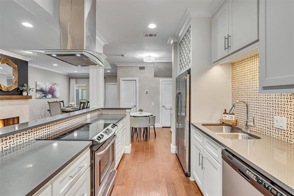 Modern kitchen featuring stainless steel appliances, light-colored cabinetry, wood-finish flooring, and a patterned tile backsplash