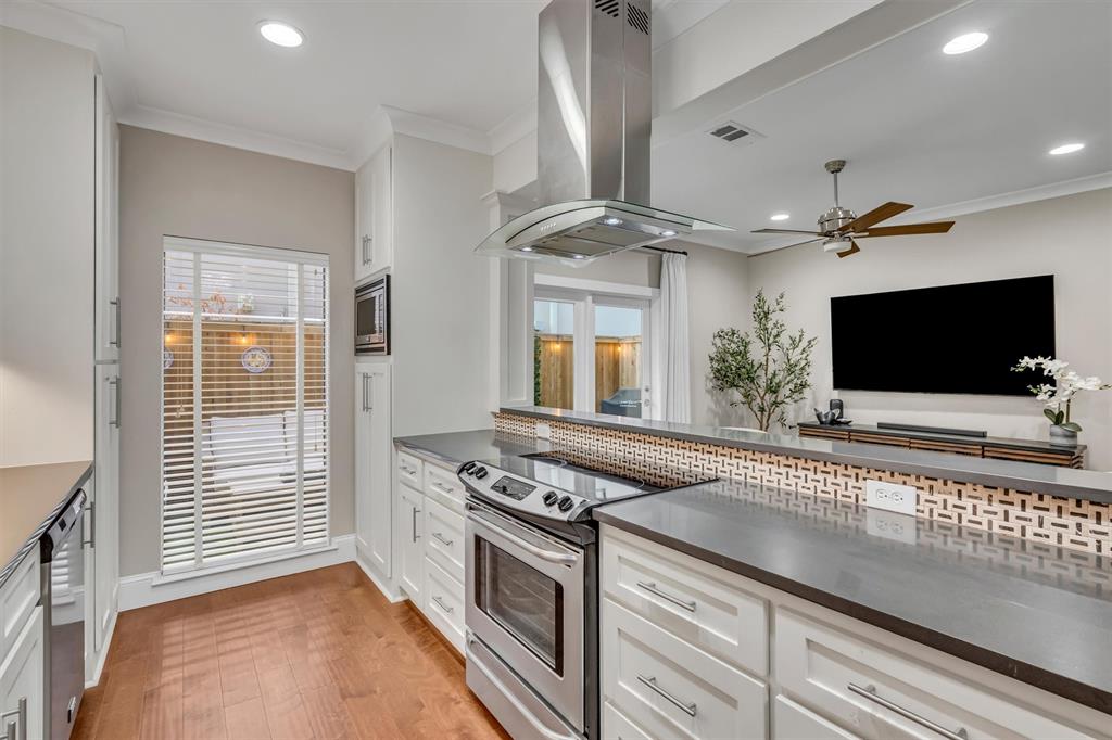Modern kitchen featuring stainless steel appliances, white cabinetry, wood-finish flooring, and a decorative tile backsplash