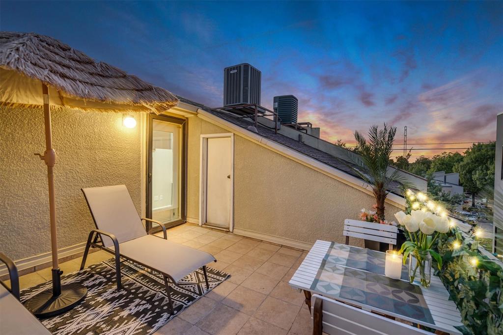 Outdoor patio with tile flooring, wall-mounted exterior lighting, and a glass-paneled entry door