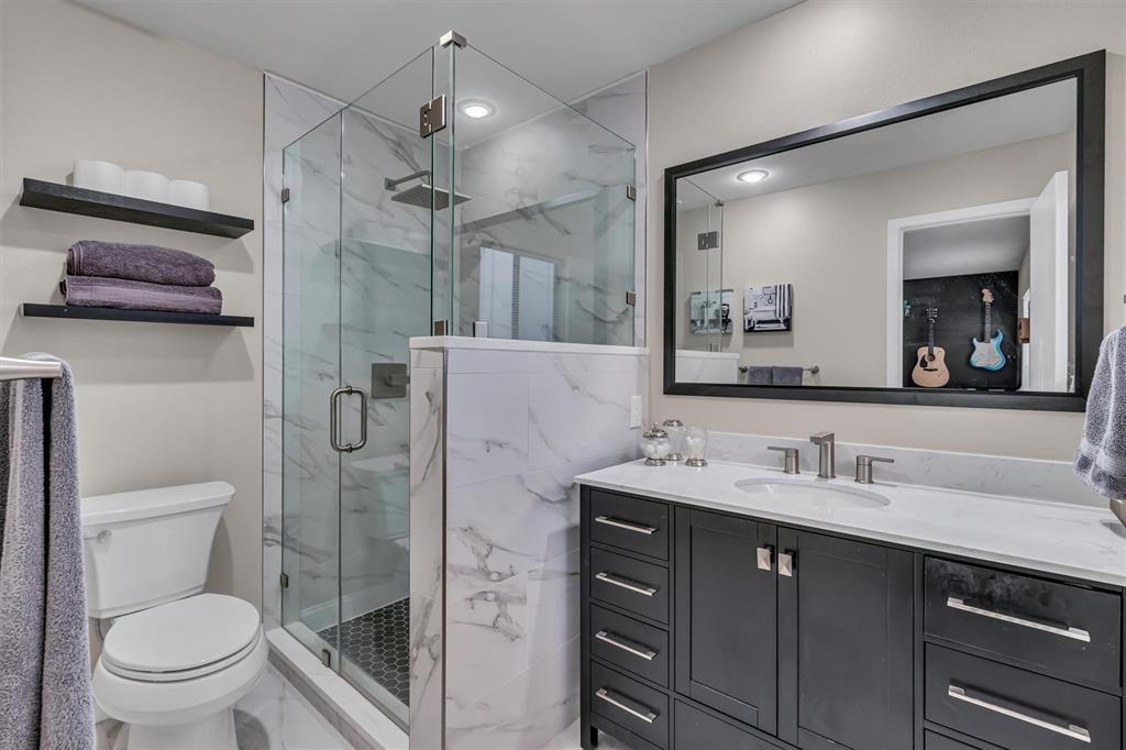 Walk-in shower with clear glass enclosure and hexagon tile flooring, complemented by a vanity with dark wood cabinetry and a light-toned countertop