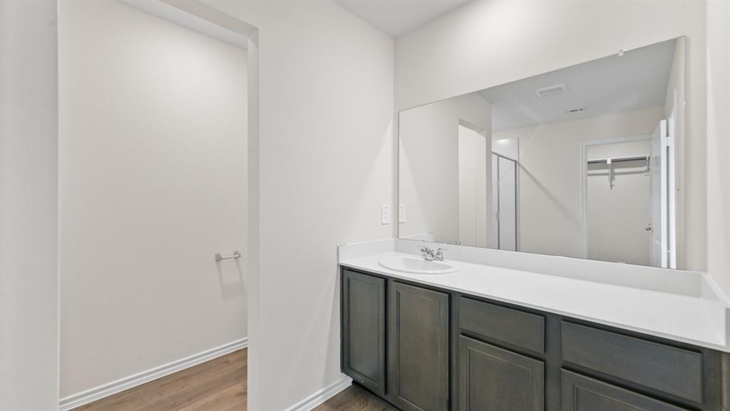 White single vanity with dark wood-finish cabinetry, a large wall-mounted mirror, and wood-finish flooring