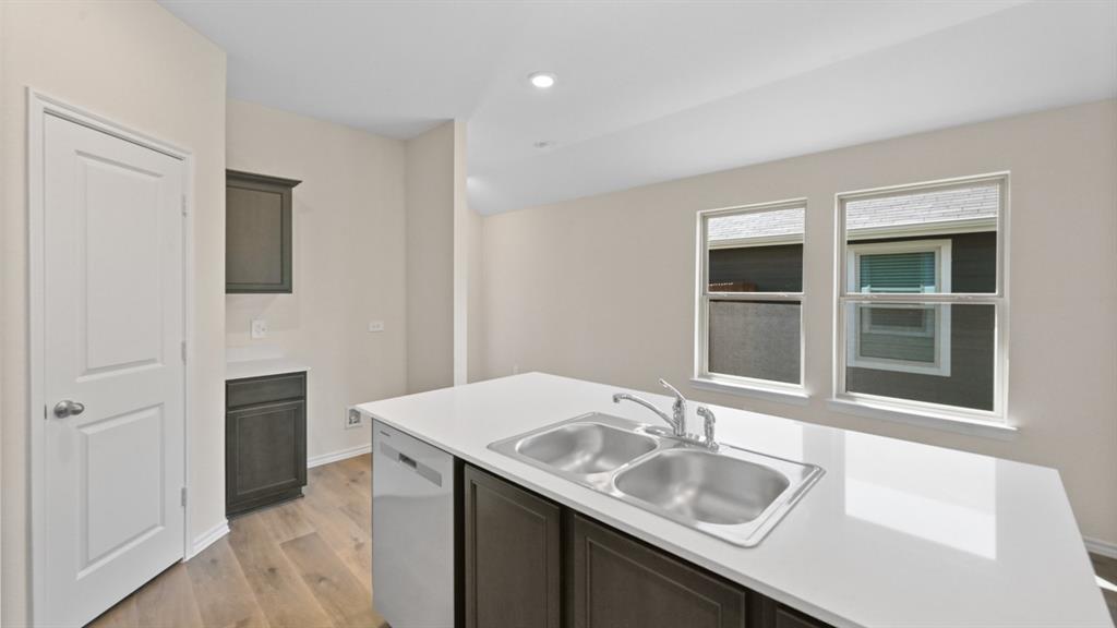 Kitchen island with a double basin stainless steel sink, solid surface countertop, wood-finish flooring, recessed lighting, and a built-in dishwasher