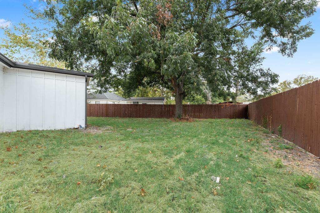 Expansive grassy yard with mature trees and a perimeter privacy fence