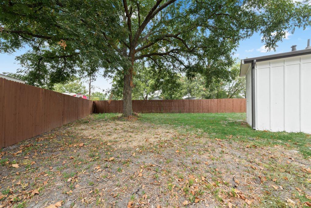 Expansive backyard featuring a mature shade tree, a wooden privacy fence, and a white exterior wall with vertical paneling