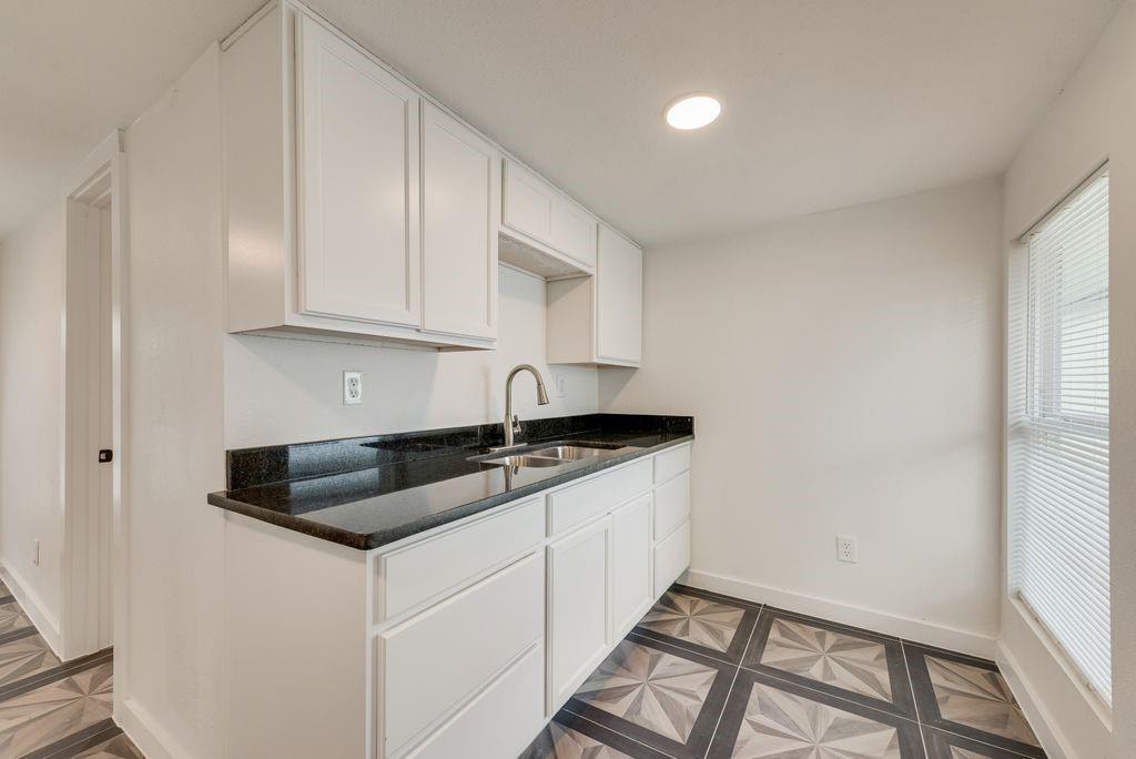 White cabinetry with dark countertops, stainless steel sink with gooseneck faucet, and patterned flooring