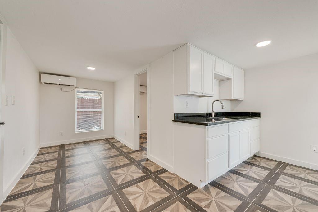 Guest Quarters Compact kitchen area with white cabinetry, dark countertops, and a stainless steel sink
