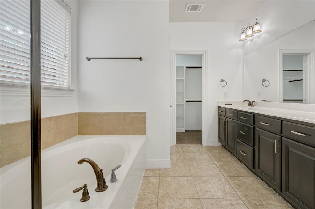 Soaking tub with bronze-finish fixtures, tile flooring, and a double vanity with dark cabinetry and a white countertop