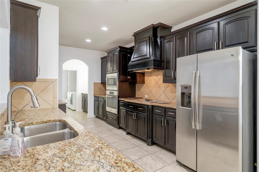 Kitchen featuring dark wood-finish cabinetry, granite-style countertops, stainless steel appliances, and a tiled backsplash