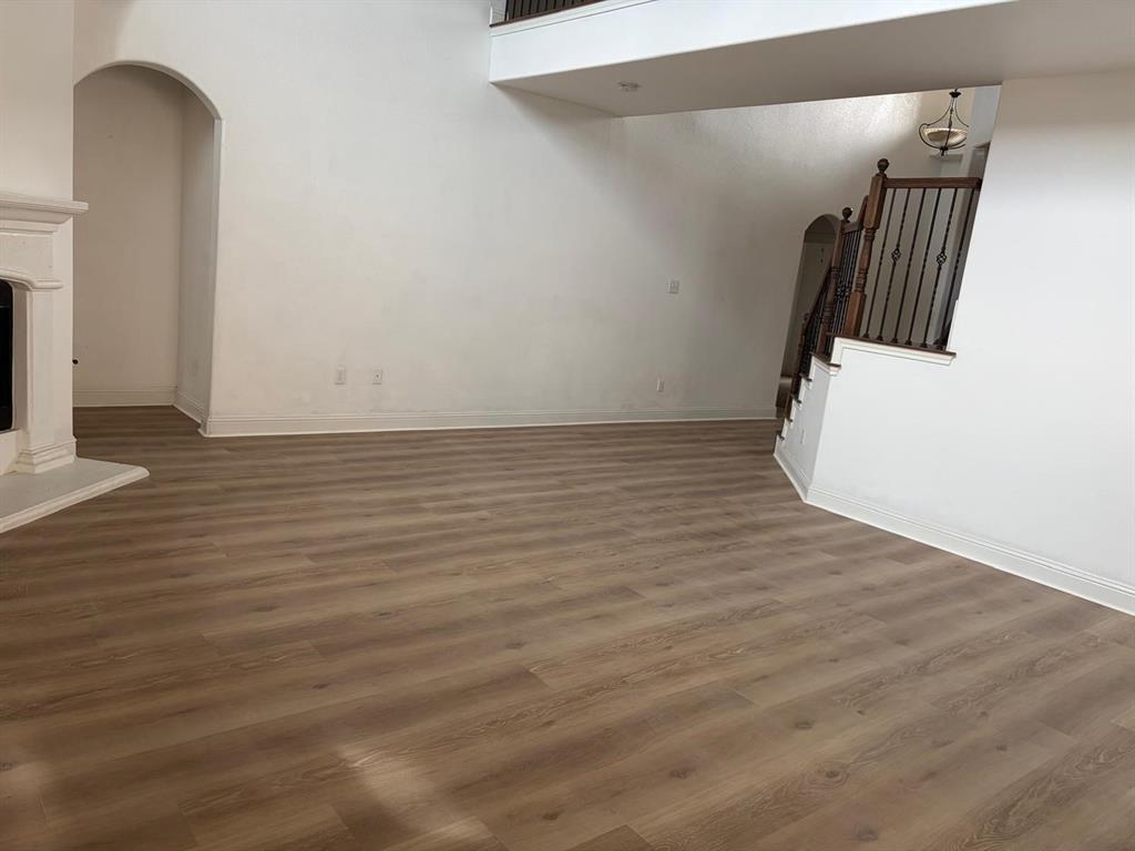 Spacious room featuring wood-finish flooring, a white mantel, and an arched doorway