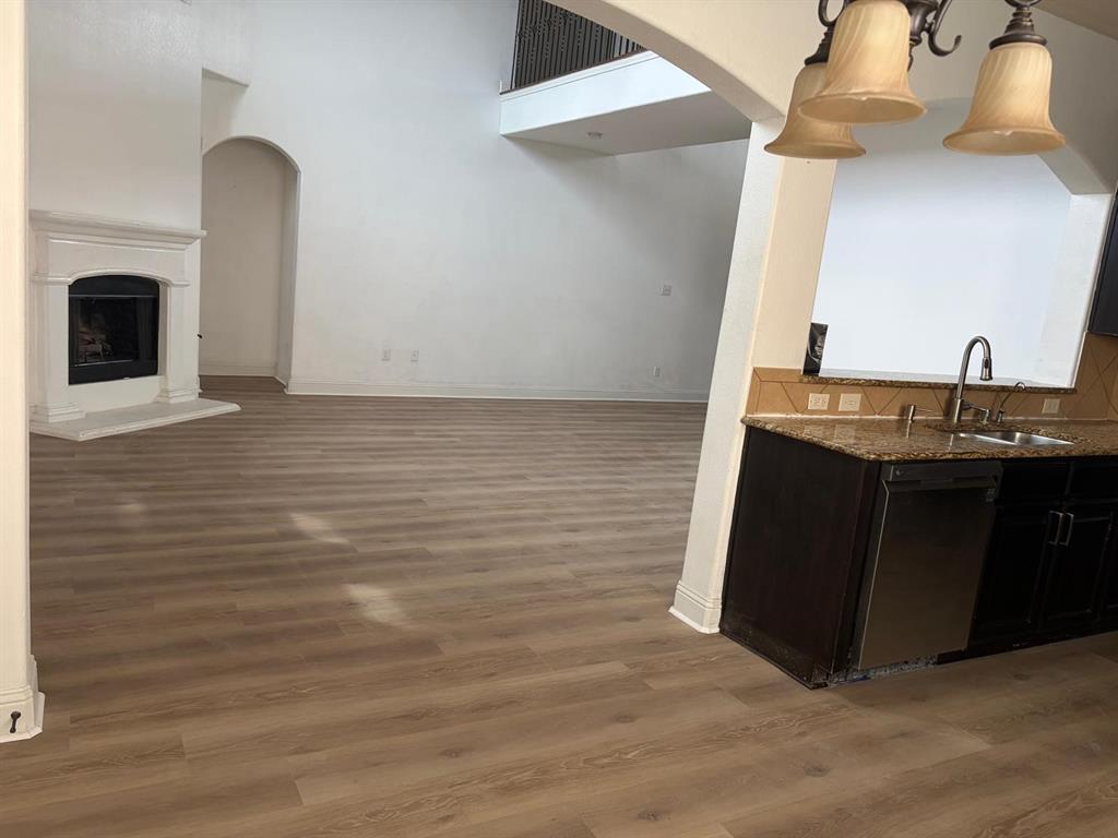 Spacious living area featuring wood-finish flooring, a traditional fireplace with a white mantel, and an arched doorway