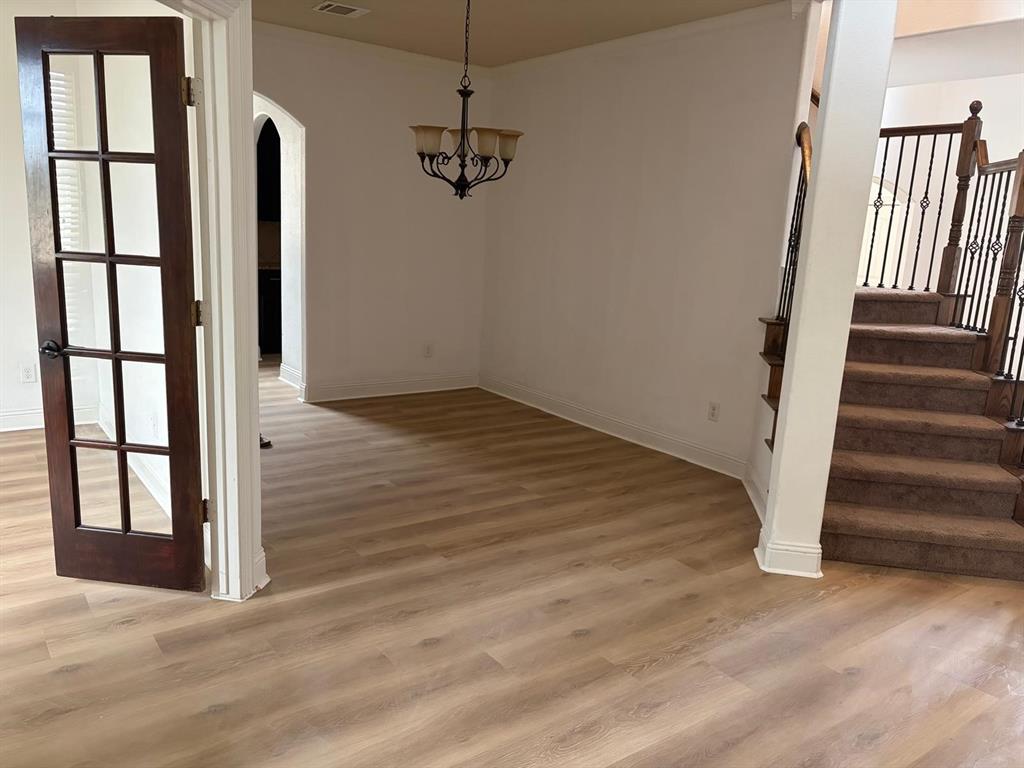 Wood-finish flooring, dark wood French door with glass panels, arched entry, wrought iron staircase balusters, and a decorative chandelier